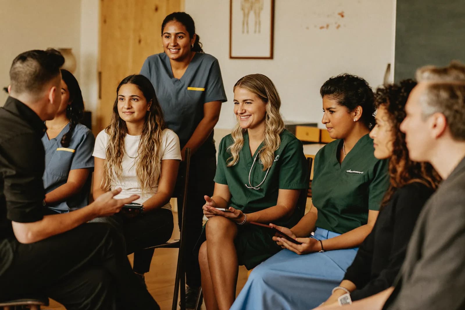 A small classroom discussion among a diverse mix of adult healthcare students seated in a semicircle with their instructor
